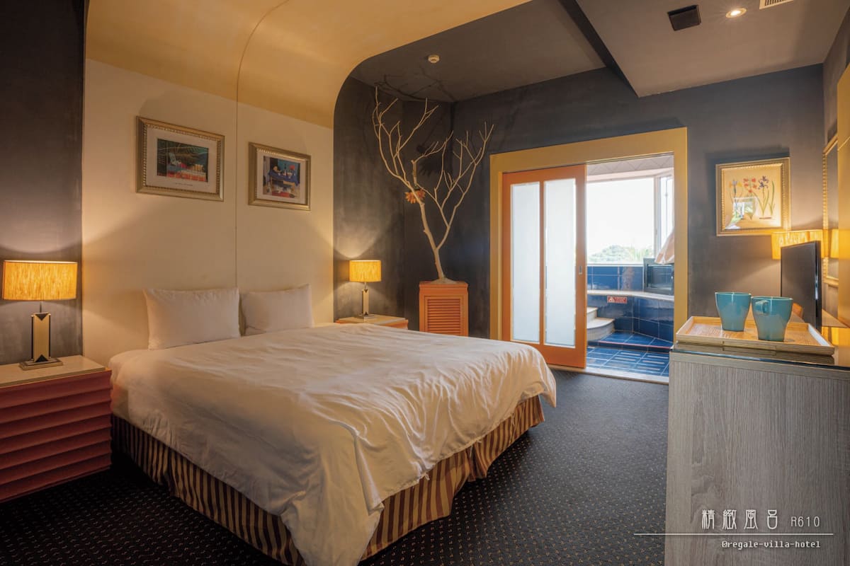 Een hotelkamer met een bed, nachtlampjes, een dressoir en uitzicht.