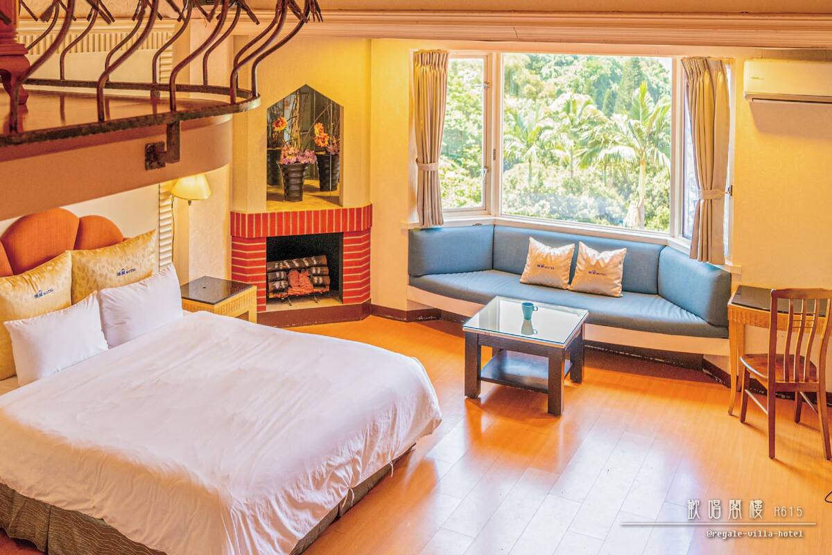Een hotelkamer met een groot bed, een bank, een bijzettafeltje en een open haard.