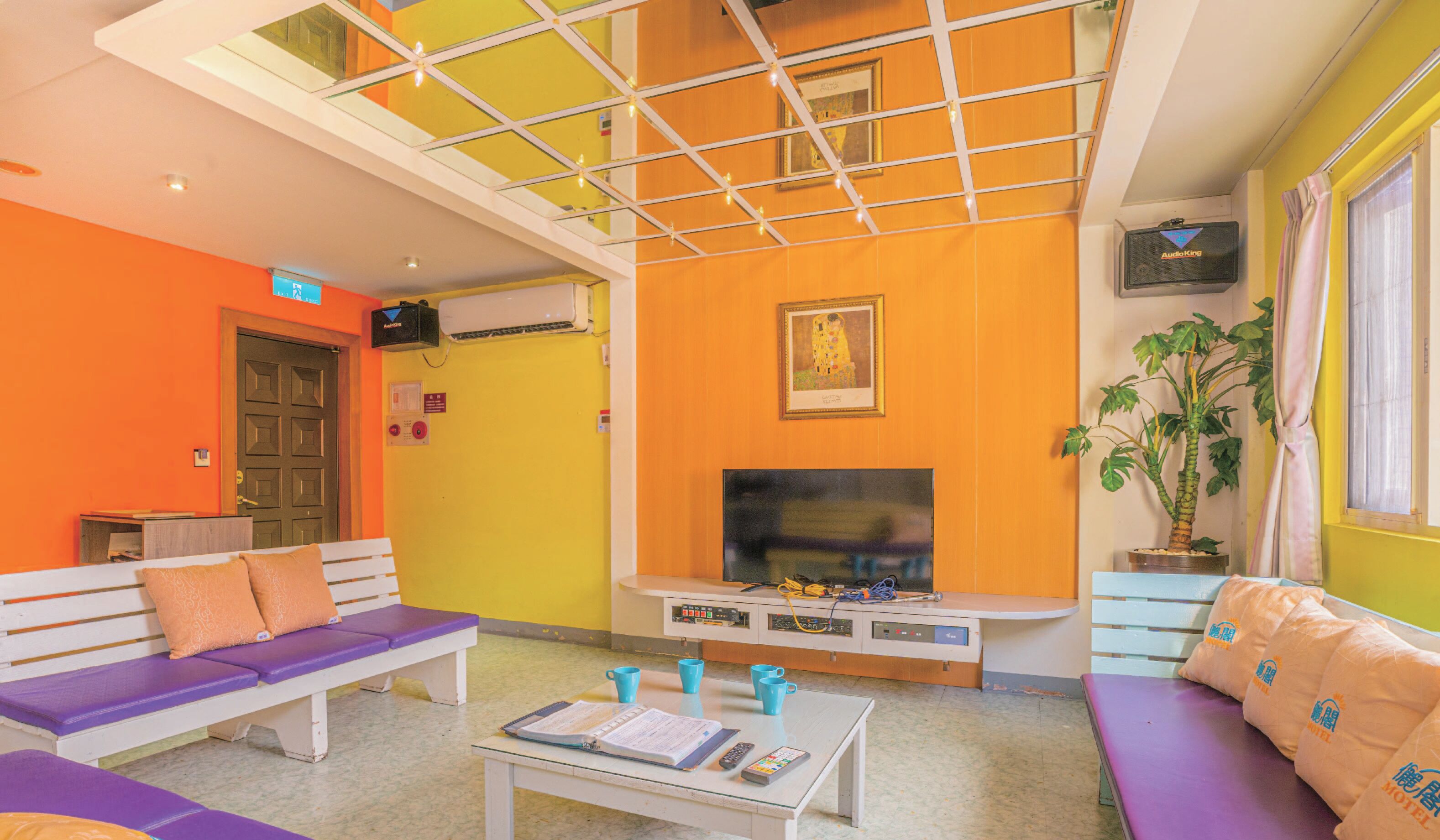 A hotel lobby with a high ceiling, a television, seating areas, and a reception desk.