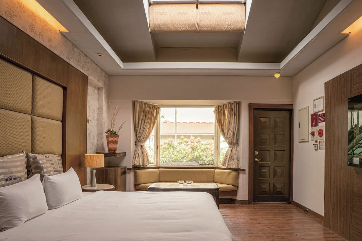 Een hotelkamer met een groot bed, een zithoek, een raam met gordijnen en een deur met een bordje.