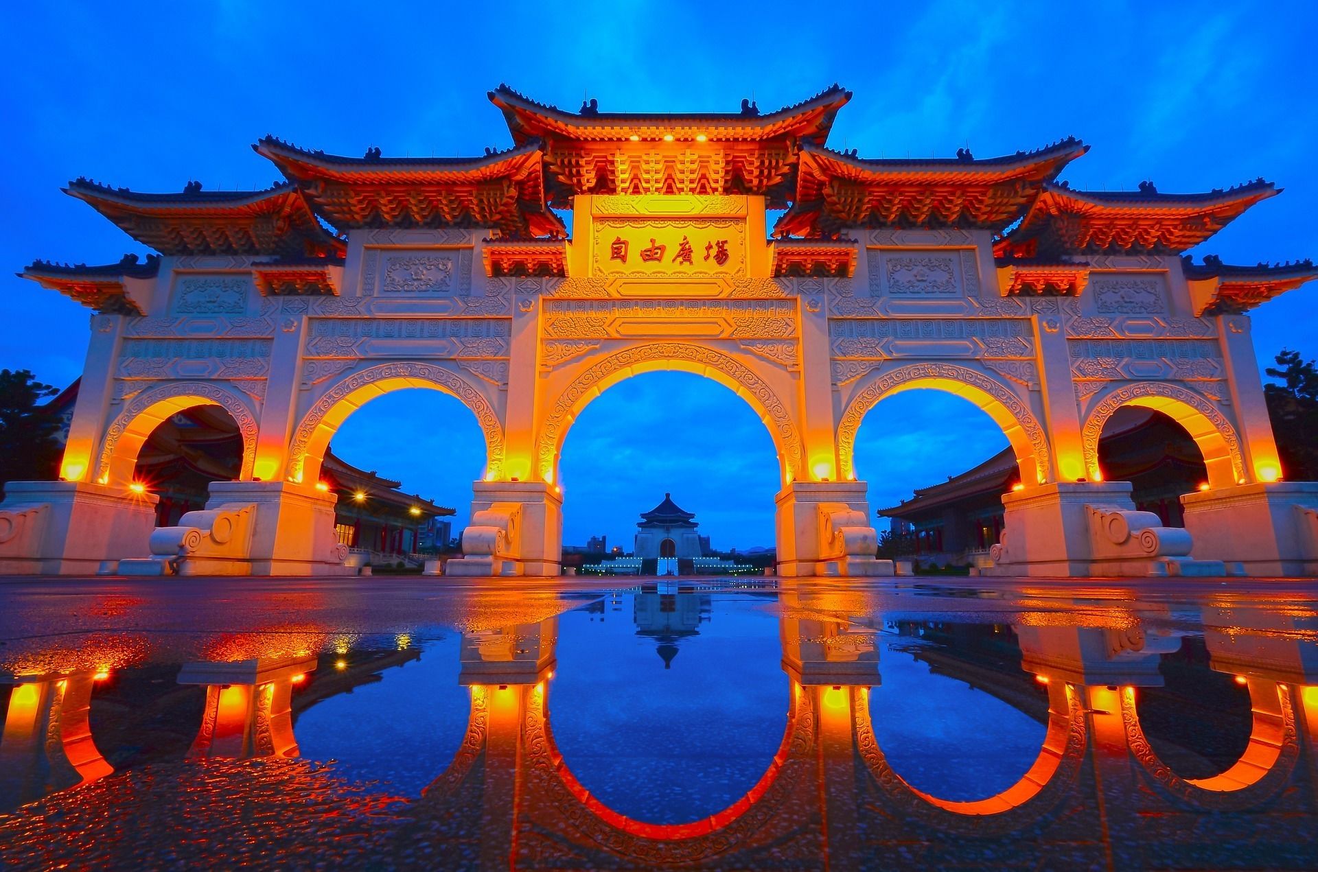 A traditional Chinese gate with intricate carvings and a reflection in the water.