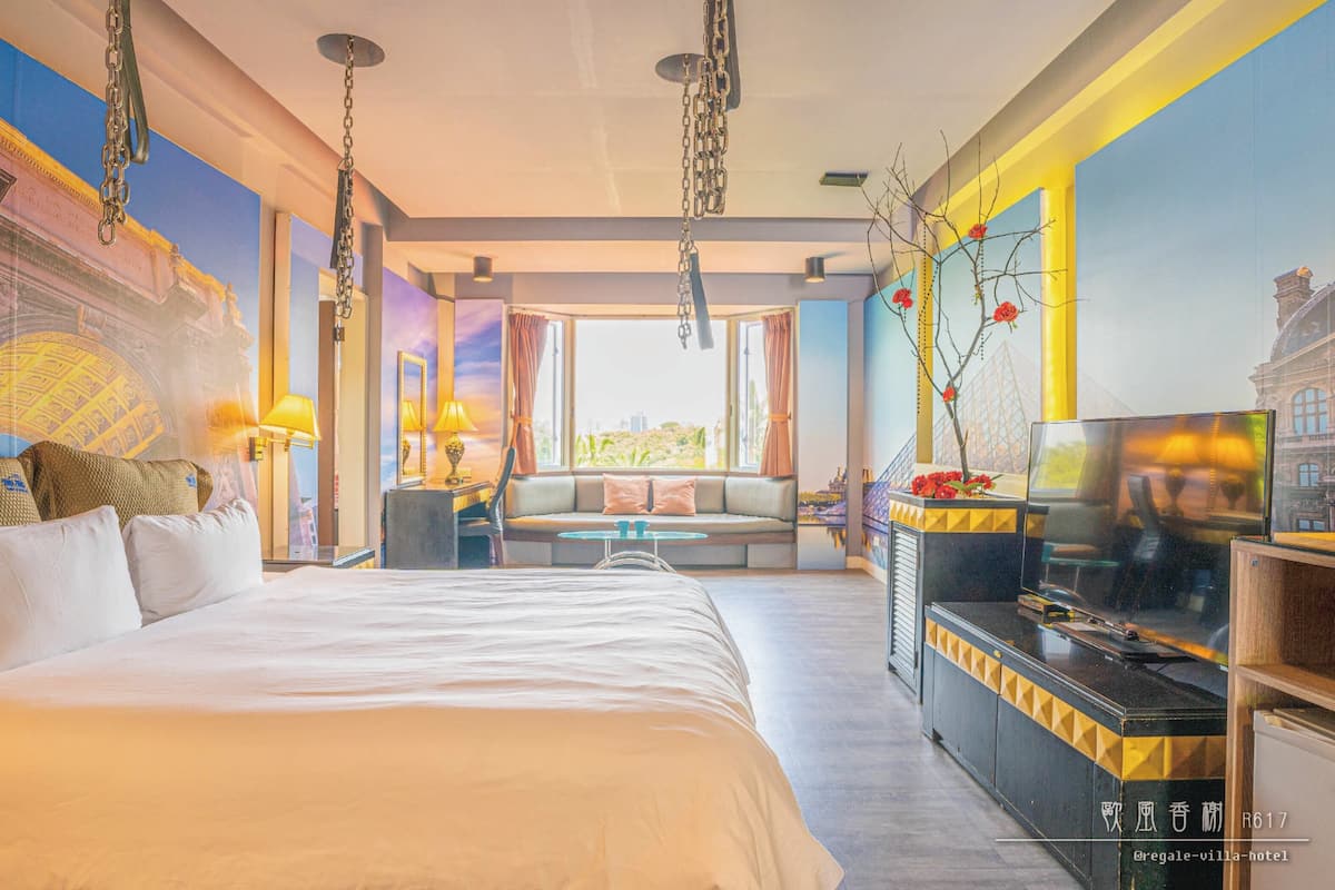 Een hotelkamer met een groot bed, een bank, een televisie en uitzicht op de stad.