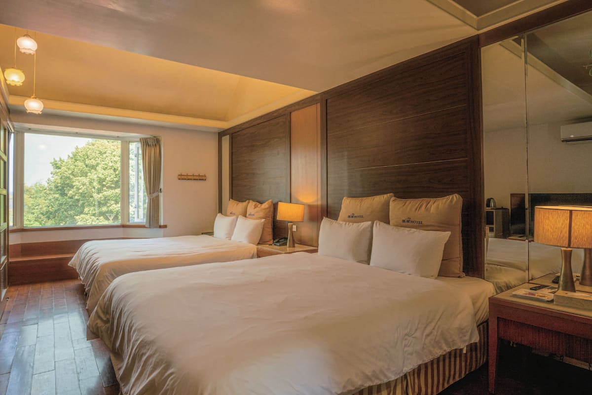 Een hotelkamer met twee bedden, een grote spiegel, een nachtkastje met lamp en een raam met gordijnen.