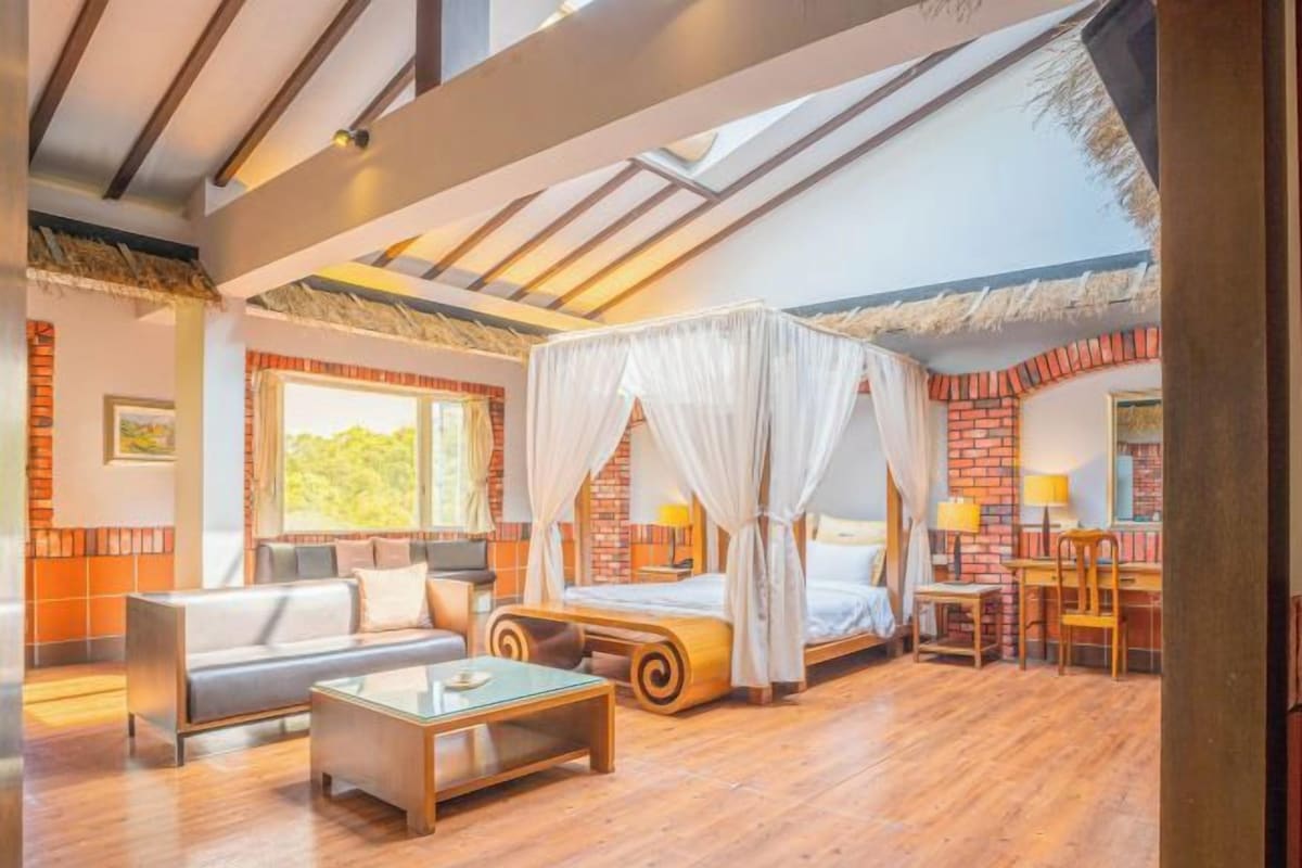 A spacious room with a large bed, a sofa, a coffee table, and a desk with chairs.