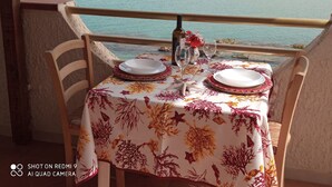 A table set for two with a floral tablecloth, a bottle, and glasses, overlooking a coastal view.