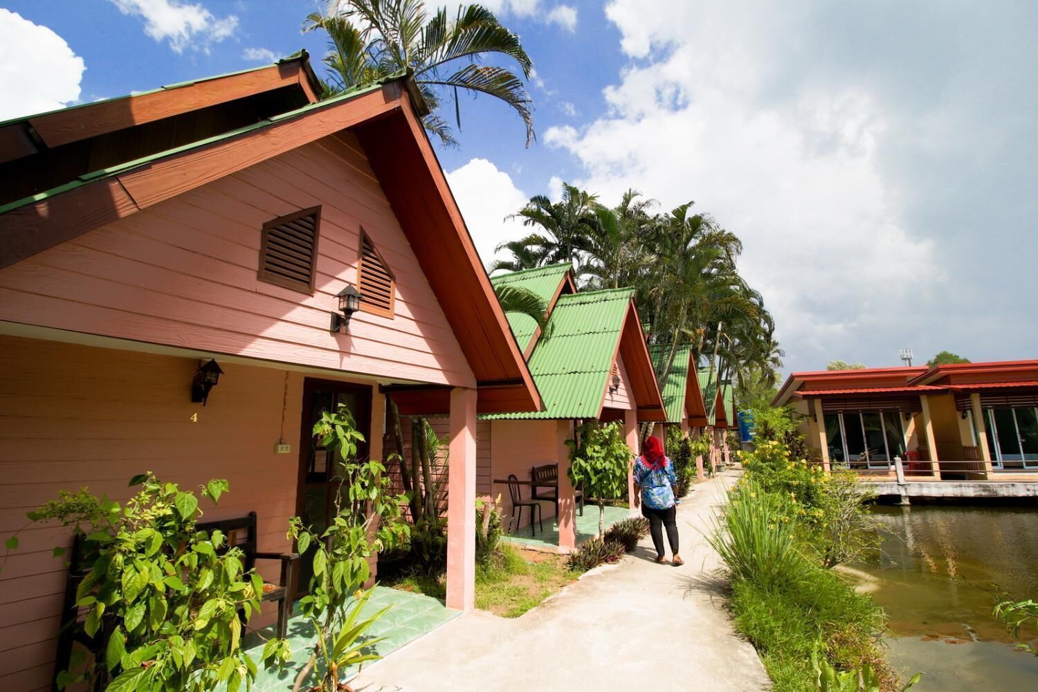 Een rij rozebungalows met een pad dat naar een waterpartij leidt, omgeven door groen.