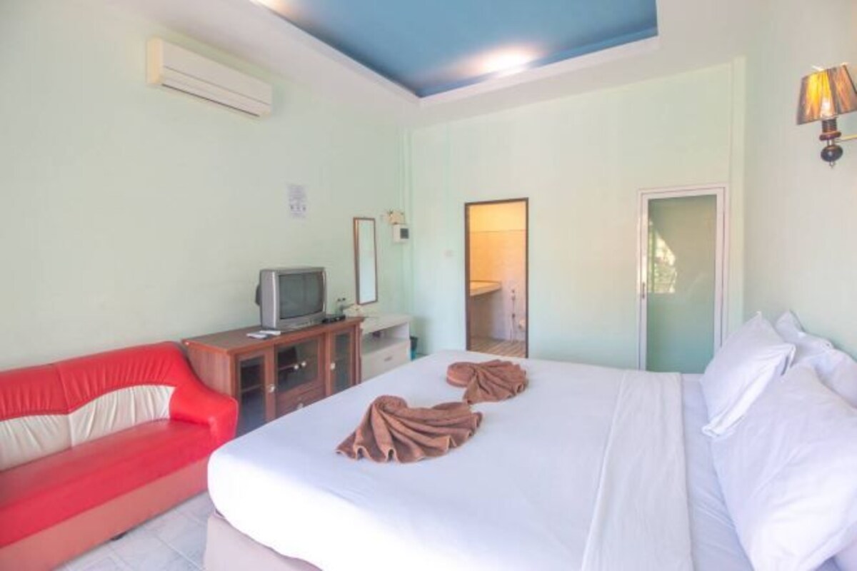 A hotel room with a bed, a red sofa, a TV on a wooden stand, and a mirror on the wall.