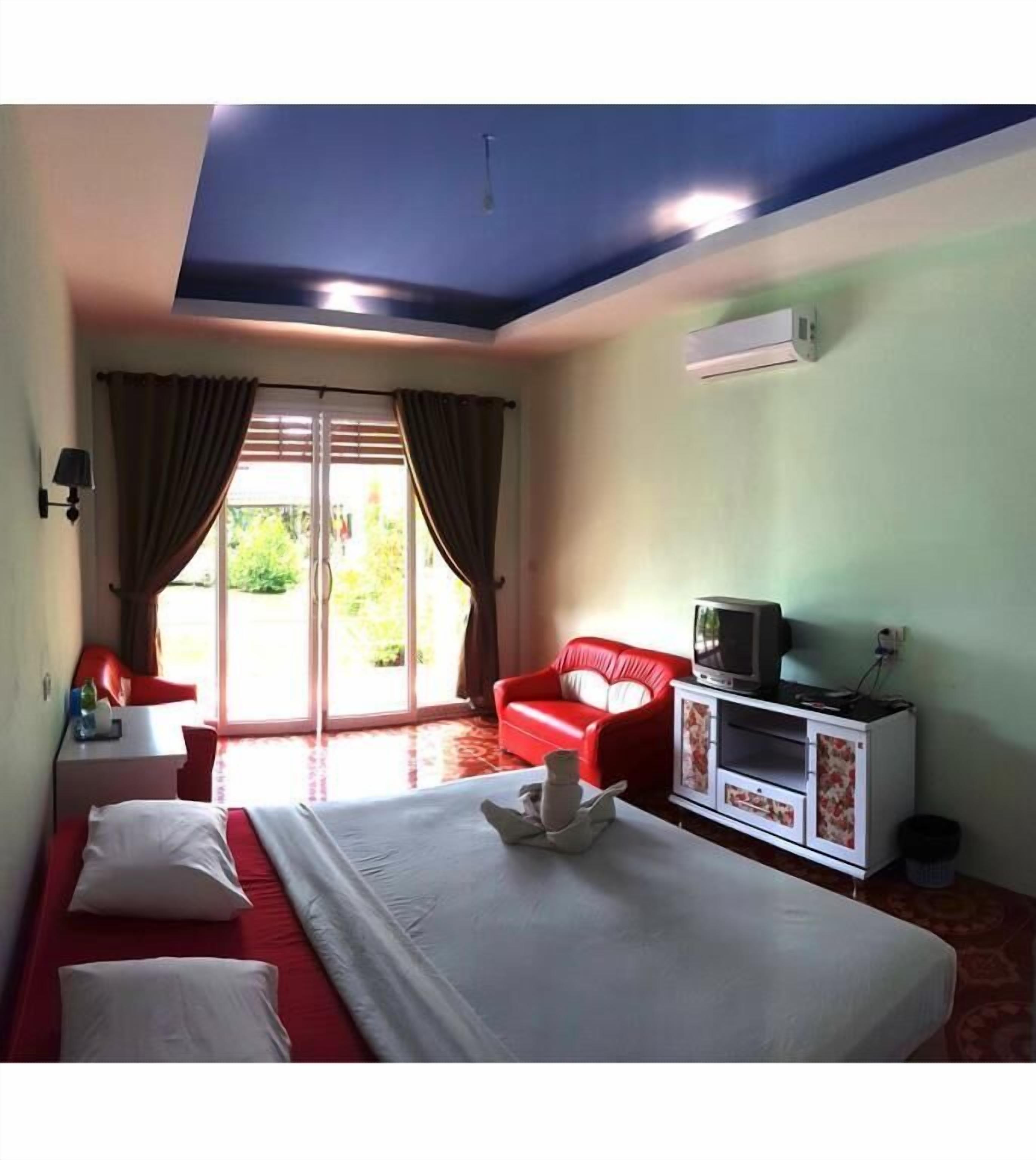 Habitación de hotel con cama, sofá rojo, televisor sobre un mueble y aire acondicionado en la pared.