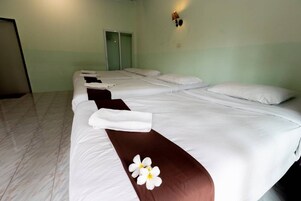 Habitación de hotel con cuatro camas dispuestas en fila, cada una con ropa blanca y un cojín marrón decorativo.