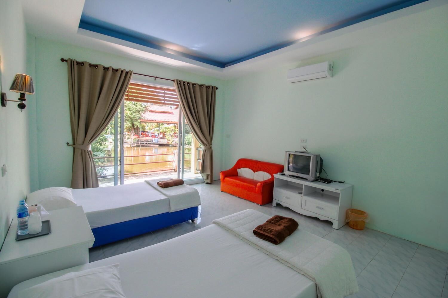Una habitación de hotel con dos camas, un televisor, un sofá rojo y una ventana con cortinas.