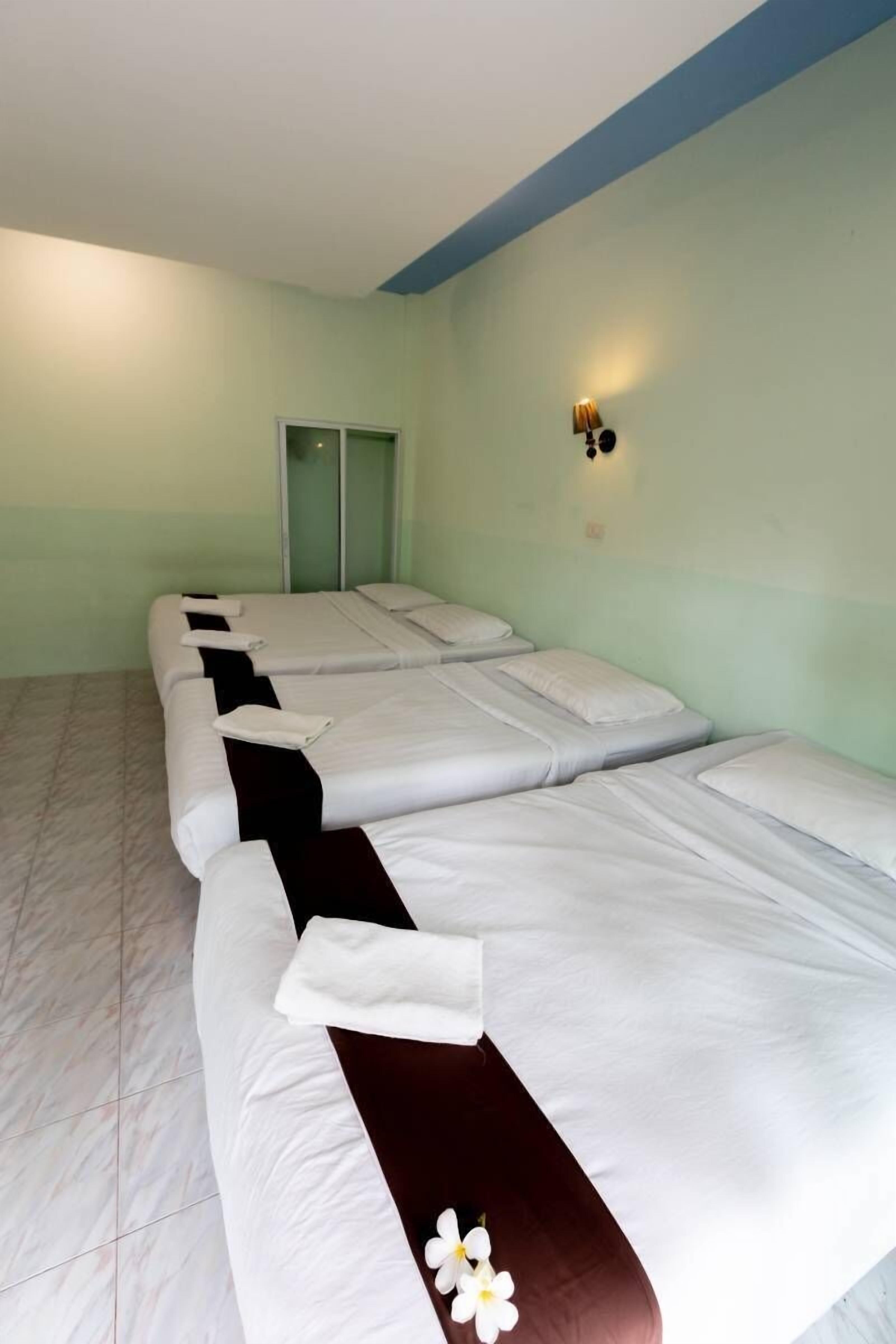 A room with four beds aligned in a row, each with white bedding and a dark brown accent.