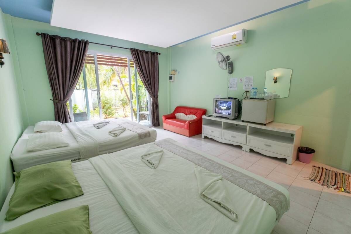 Una habitación con dos camas, un televisor, un pequeño sofá rojo y un armario blanco.