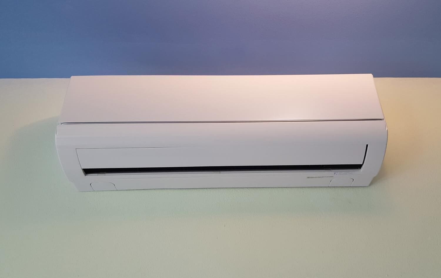 A white air conditioning unit on a light-colored surface against a blue wall.