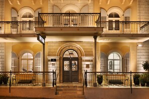 Una entrada majestuosa amb una doble escala que condueix a un balcó, flanquejada per finestres d'arc i una porta central amb una reixa de ferro decorativa.