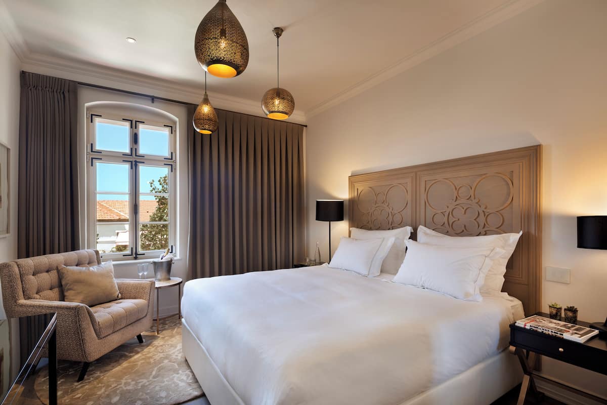 Une chambre d’hôtel spacieuse, dotée d’un grand lit, d’un coin salon avec un fauteuil, une petite table et une fenêtre avec des rideaux.