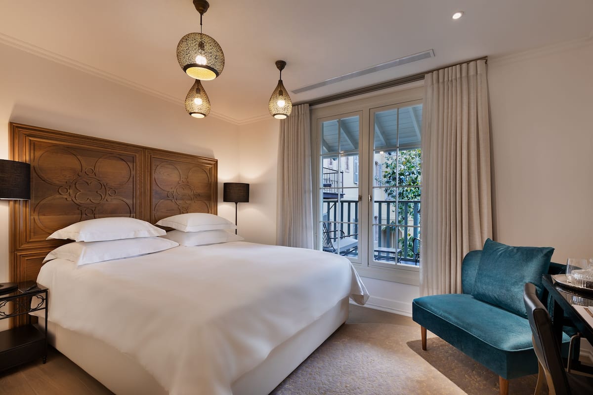 Une chambre d’hôtel avec un grand lit, un bureau avec une chaise et un balcon avec des rideaux.