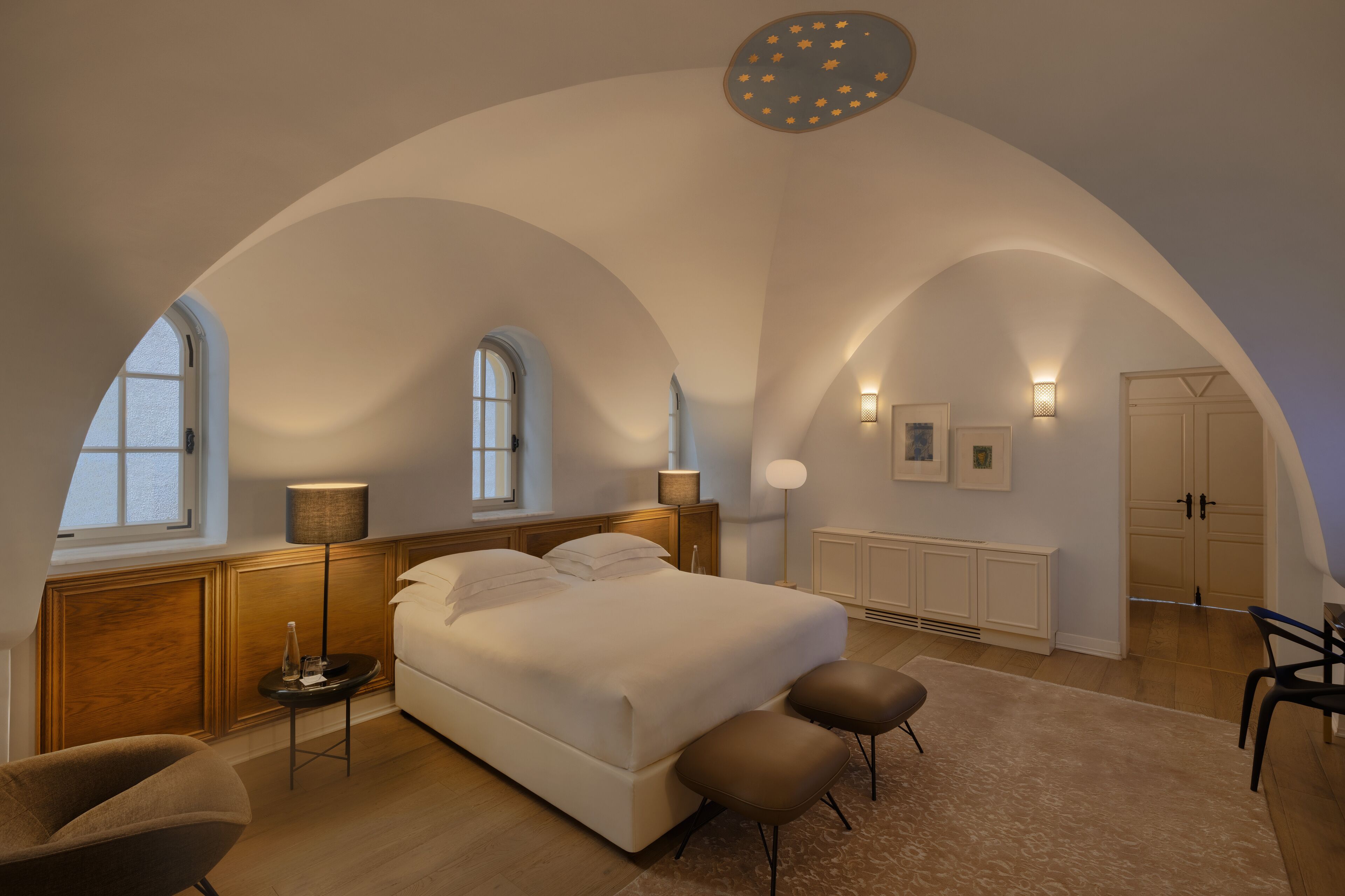 A bedroom with a large bed, two side tables, a chair, and a ceiling light fixture.