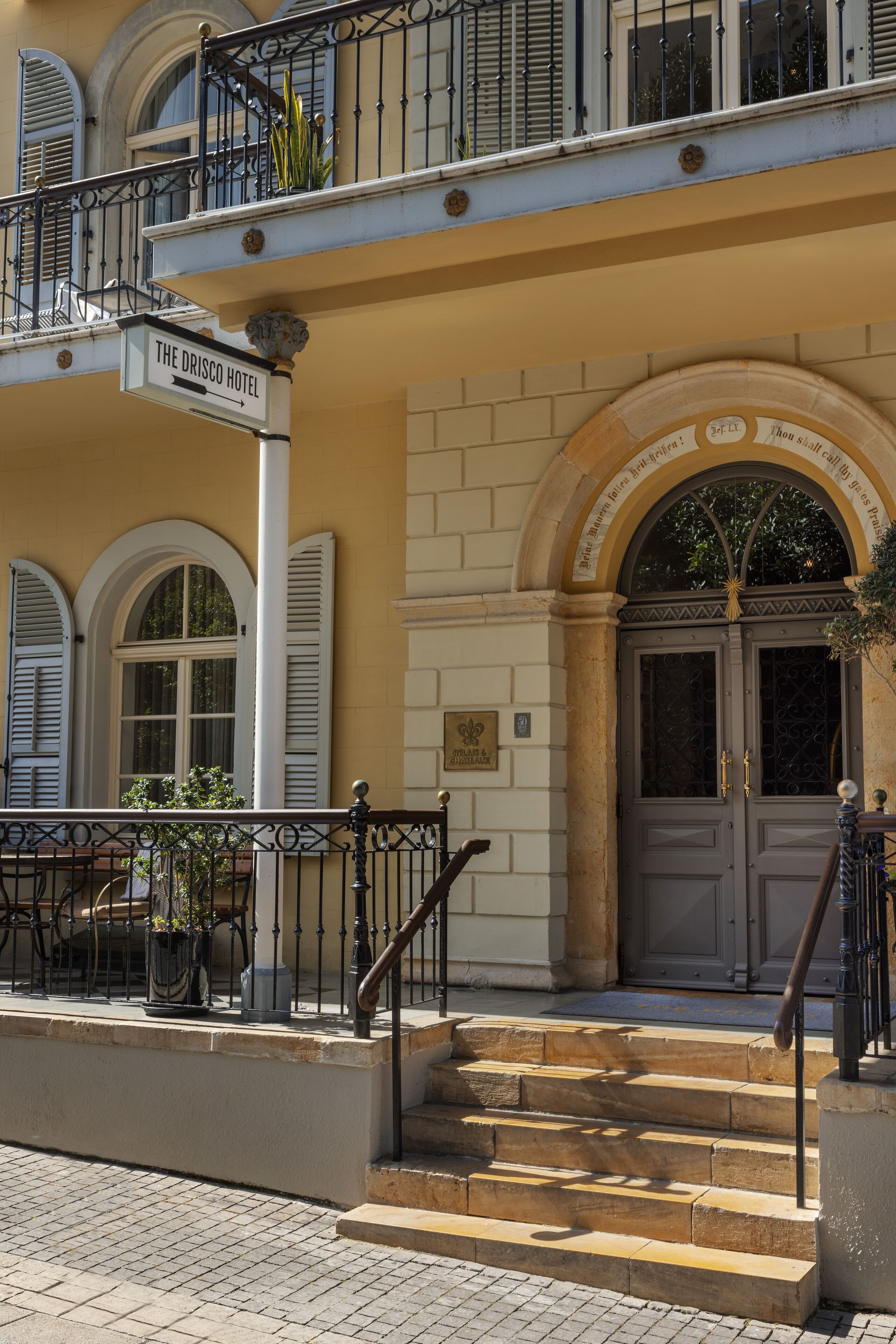 A hotel entrance with a sign reading "The Drisco Hotel," a set of stairs leading to the door, and a balcony with a railing.