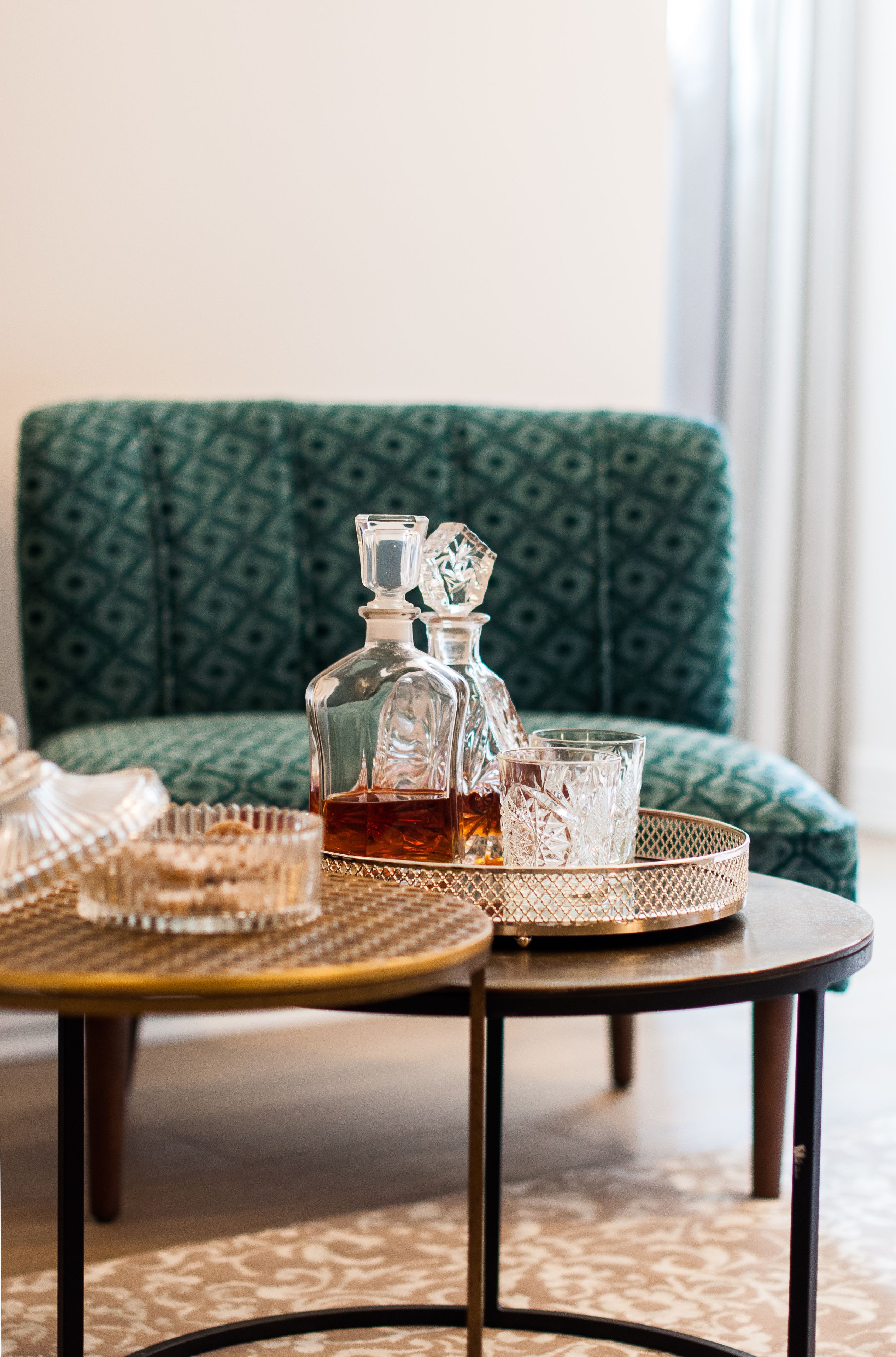 A room with a patterned green sofa, a small round table with a tray holding a decanter, glasses, and a cake.