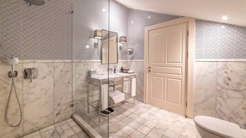 Un baño con ducha envuelta en vidrio, un lavamanos con espejo y un inodoro.