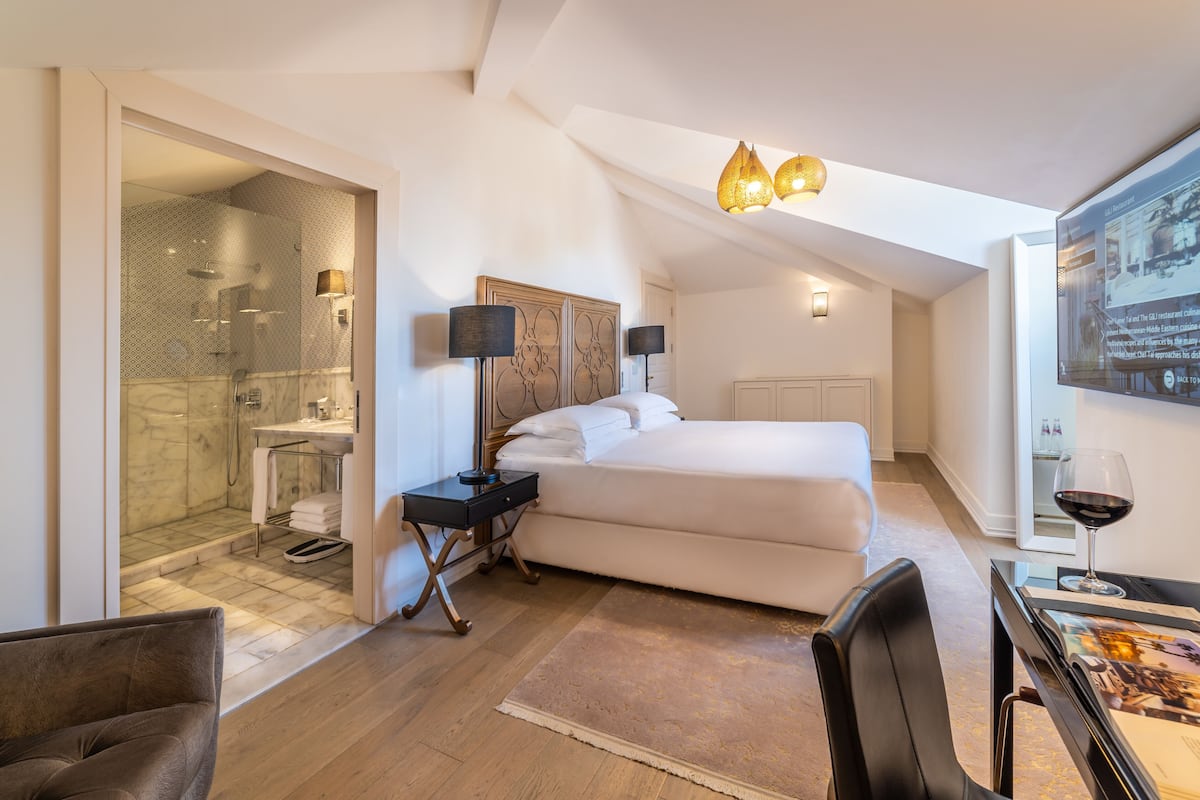 Une chambre d’hôtel moderne, dotée d’un grand lit, d’un bureau avec une chaise, d’un espace douche et d’un tableau au mur.