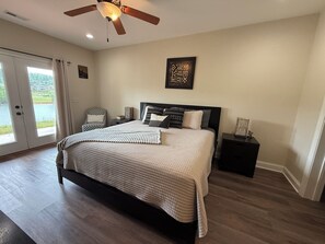 A bedroom with a bed, a ceiling fan, a nightstand, a framed artwork, and a view through a glass door. - Beautiful lake front house, pool table, and fire pit, kayaks,Fall price discount (Hiawassee)
