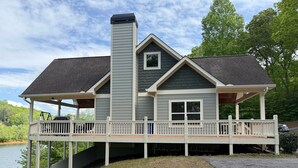 A two-story house with a covered porch, a chimney, and a view of a lake. - Beautiful lake front house, pool table, and fire pit, kayaks,Fall price discount (Hiawassee)