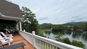 A wooden deck with white railings, outdoor furniture, and a view of a lake surrounded by trees and hills. - Beautiful lake front house, pool table, and fire pit, kayaks,Fall price discount (Hiawassee)