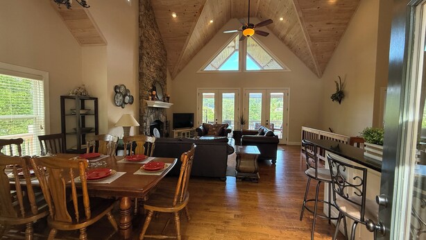 A spacious living area with a high ceiling, a fireplace, a dining table set for four, and a kitchen area with a bar. - Beautiful lake front house, pool table, and fire pit, kayaks,Fall price discount (Hiawassee)
