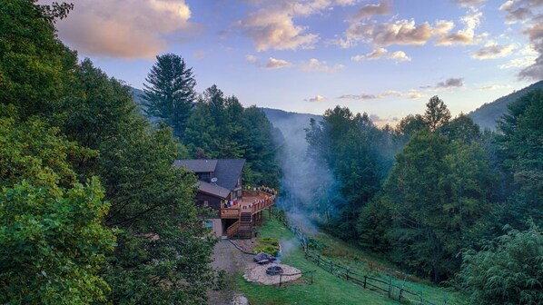 A cabin with a deck, surrounded by dense forest and a mountain backdrop. - Bliss House (Hot Springs)