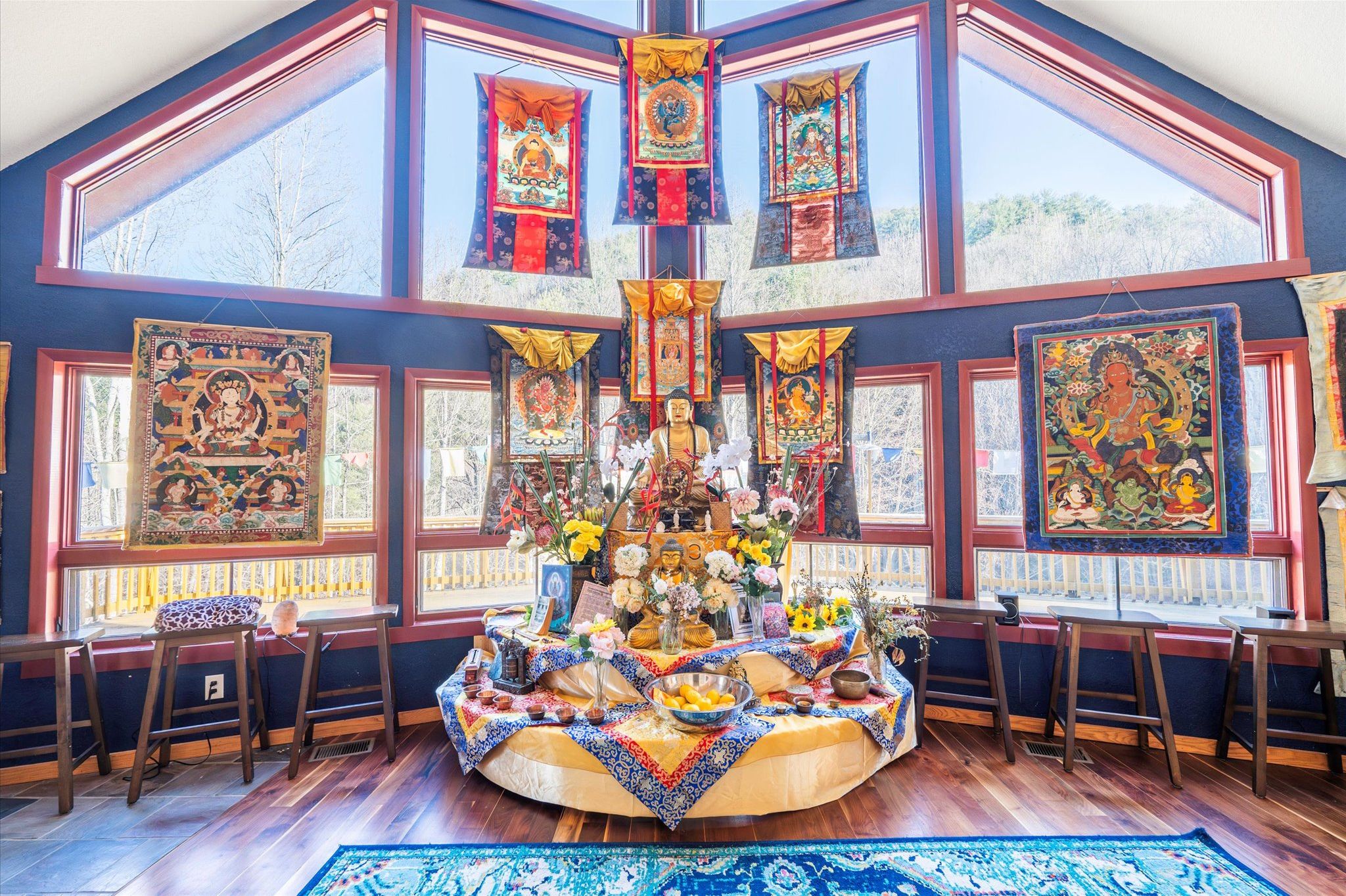 Ein Zimmer mit einem großen Fenster, einer Buddha-Statue und tibetanischer Kunst an den Wänden.