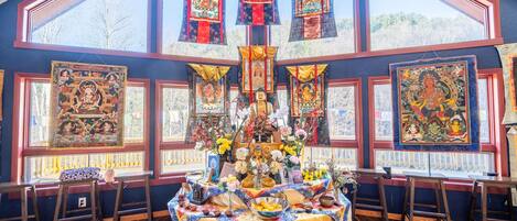 A room with a large window, a Buddha statue, and Tibetan art on the walls.