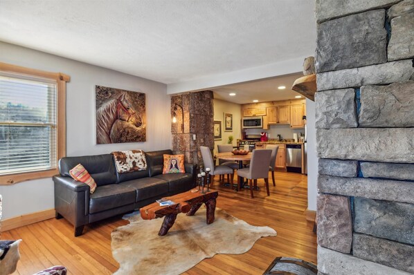 A modern living room with a black leather sofa, a wooden coffee table, and a large painting of a horse.