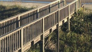 Une promenade en bois qui mène à une plage d’où l’on a une vue dégagée sur l’océan.