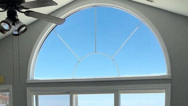 Une pièce dotée d’une grande fenêtre en arc de cercle donnant sur l’océan, d’un ventilateur de plafond et d’un canapé en cuir noir.