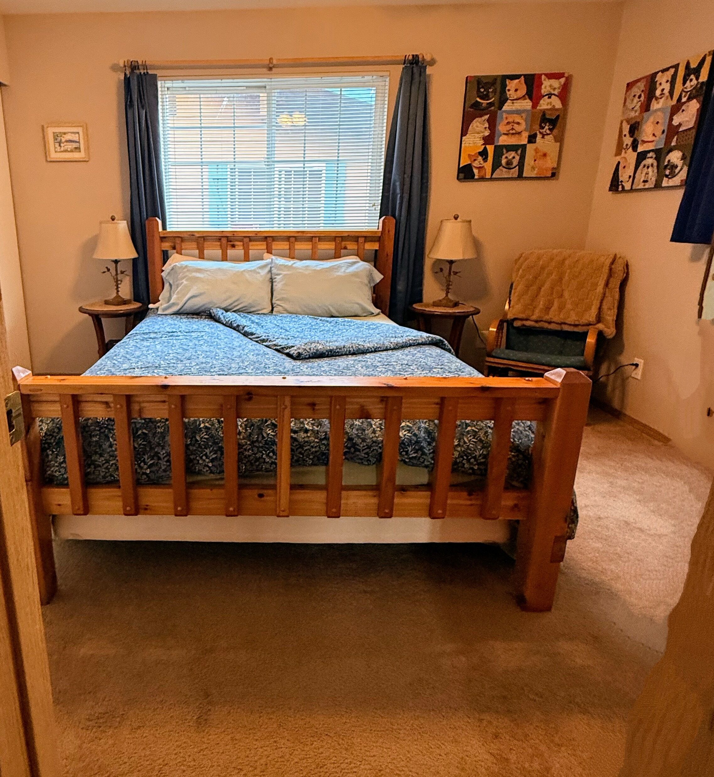 Une chambre à coucher avec un lit en bois, deux tables de chevet avec des lampes, une chaise et une fenêtre avec des rideaux.