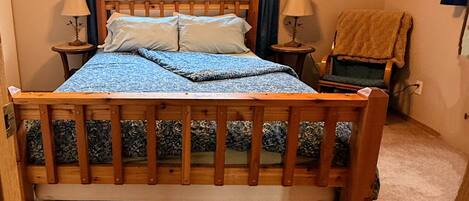 Une chambre à coucher avec un lit en bois, deux tables de chevet avec des lampes, une chaise et une fenêtre avec des rideaux.