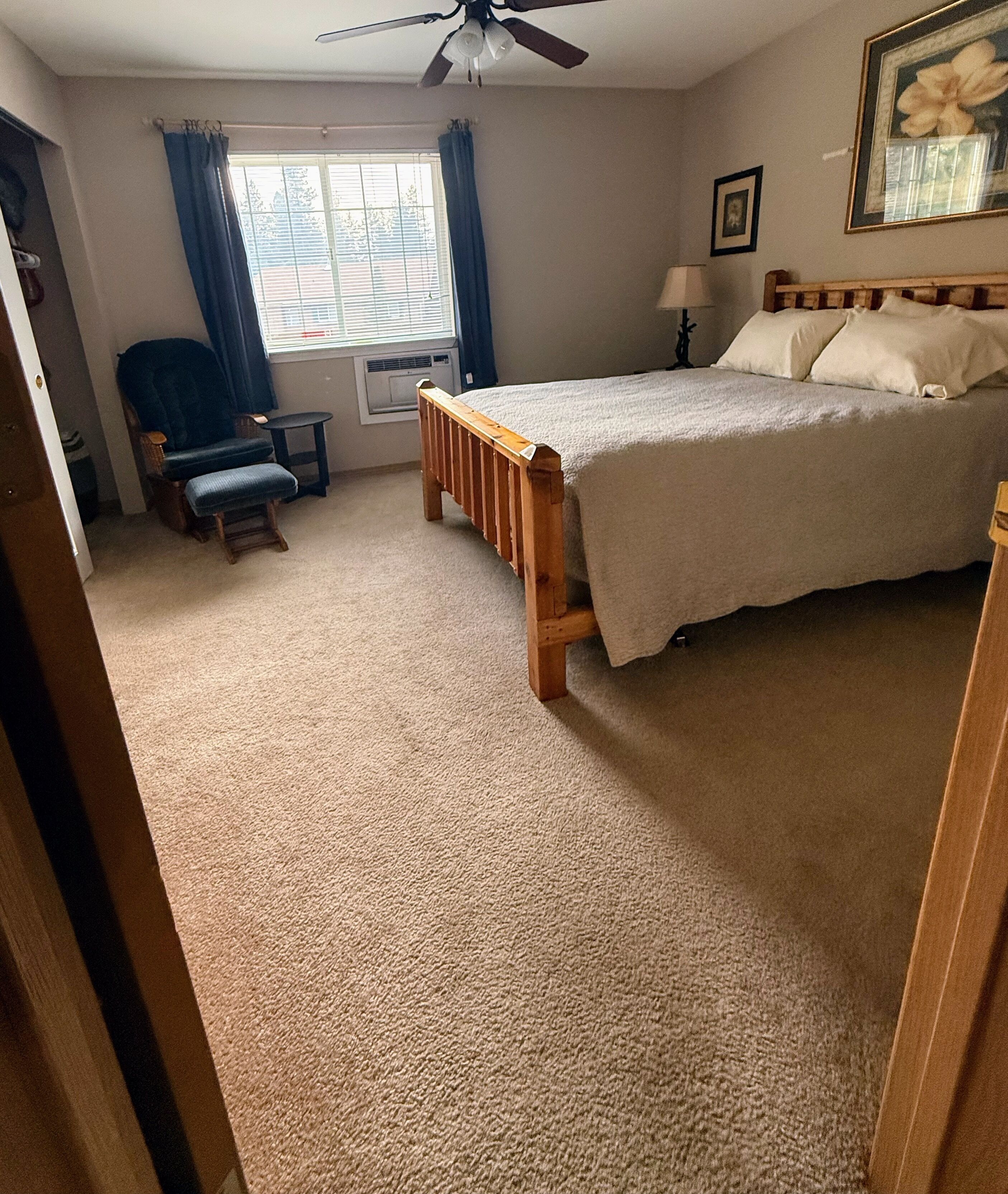 Un dormitorio con cama, una silla, una mesa y un ventanal con cortinas.