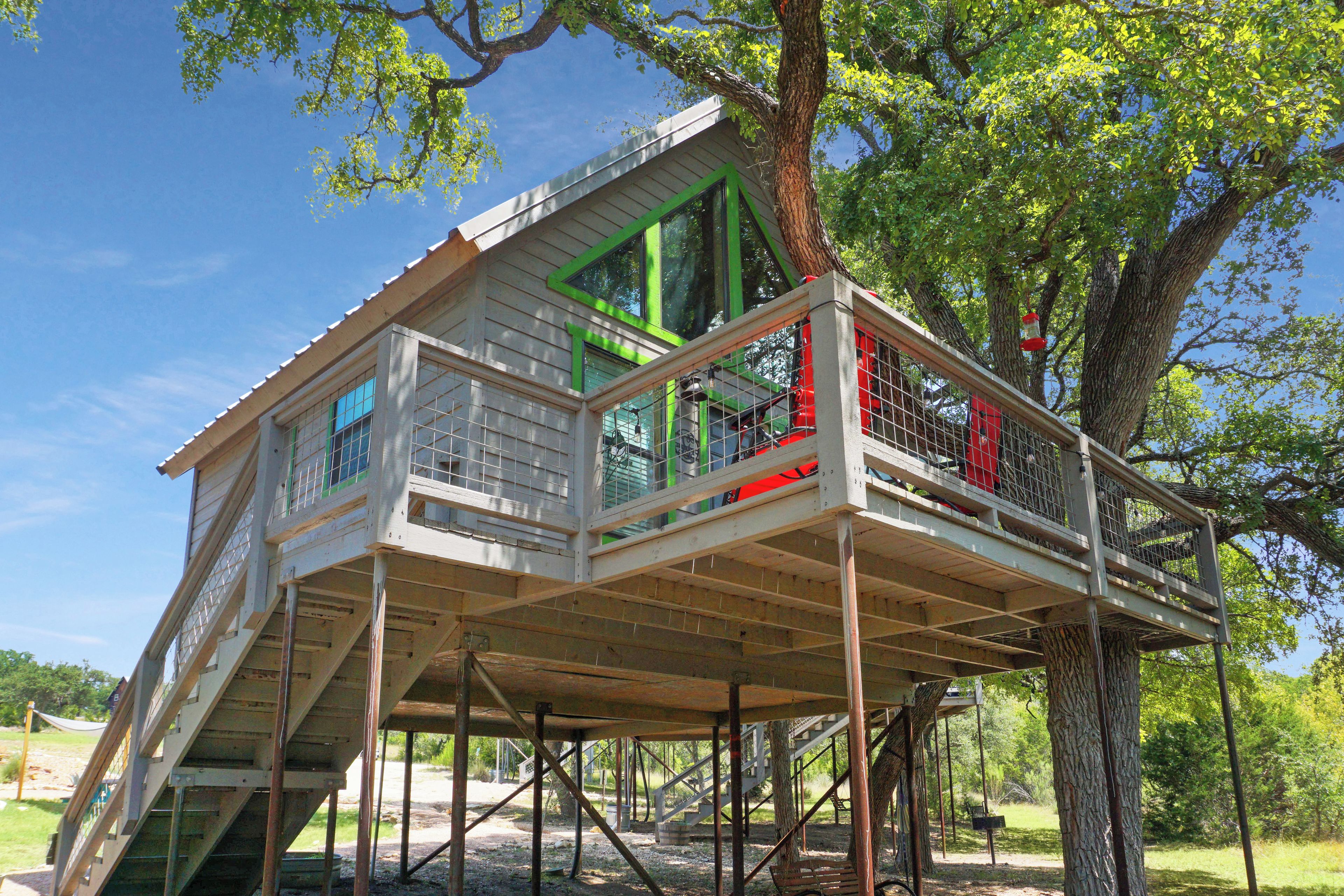 A treehouse with a wooden deck, built on stilts, and surrounded by trees.