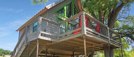 A treehouse with a wooden deck, built on stilts, and surrounded by trees.