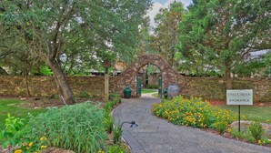 Un arc en pierre mène à un jardin où poussent des fleurs jaunes, et une pancarte indique : « Entrée des vignobles de Fall Creek ».