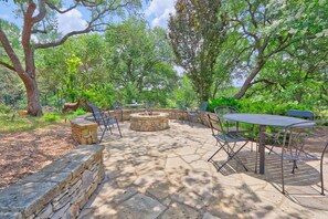 An outdoor patio with stone flooring, metal tables and chairs, and a stone fire pit. - Fall Creek Vineyards Wine Country Inn | Free Wine Tasting! (Driftwood)