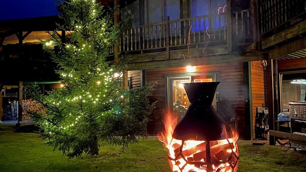 Un edificio di due piani con un balcone, un albero di Natale addobbato di luci e un elemento decorativo a forma di fuoco in primo piano.