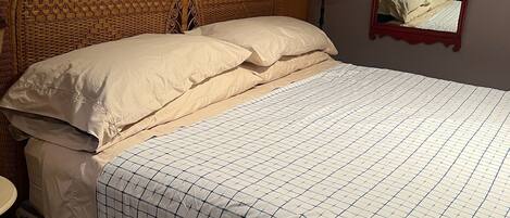 Una cama bien hecha con una colcha estampada y falda floral, un cabecero de madera y un espejo en la pared.