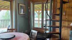 Una camera accogliente con una scala in legno, un tavolo da pranzo con sedie e ampie finestre.