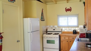 Una cocina compacta con un refrigerador blanco, estufa, armarios de madera y una ventana con persianas.
