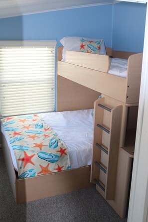 Una cama litera con una colcha estampada de estrellas, una escalera de madera y una ventana con persianas.