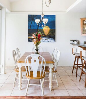 Enjoy meals in this dining area with a large table and six chairs, a beautiful painting, and a vase with a floral arrangement.