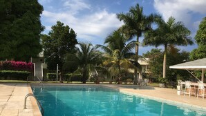 A swimming pool with a tiled deck, surrounded by palm trees and a covered seating area. - Anna's Joye Seawind - Studio Apt, Fully A/C close to beach, 24Hr Security. (Montego Bay)