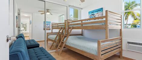 Una cama litera con escalera, un sofá azul, un ventilador de techo y un cartel en la pared.